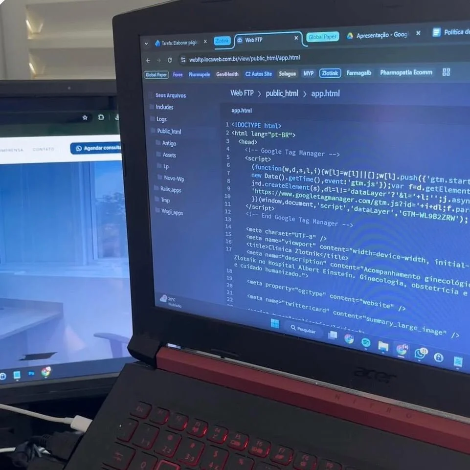 Notebook com código HTML aberto ao lado de um segundo monitor, no setup de trabalho de Ana